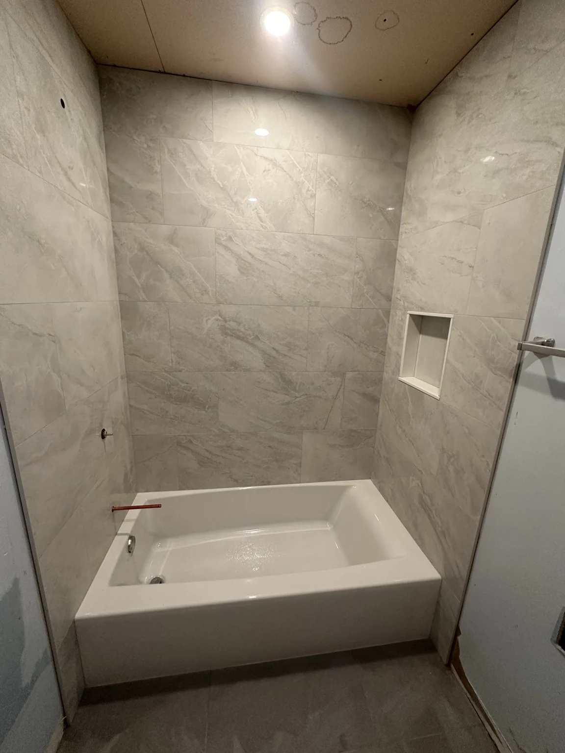 Large-format marble-look bathtub surround with recessed niche before final room finishing