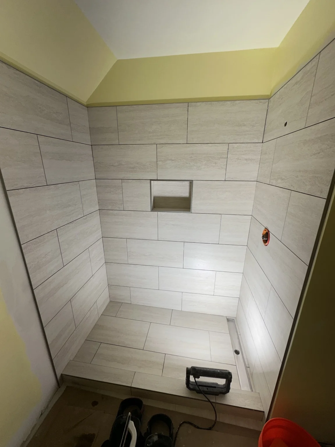 Stone-look tiled shower with recessed niche and linear drain during installation