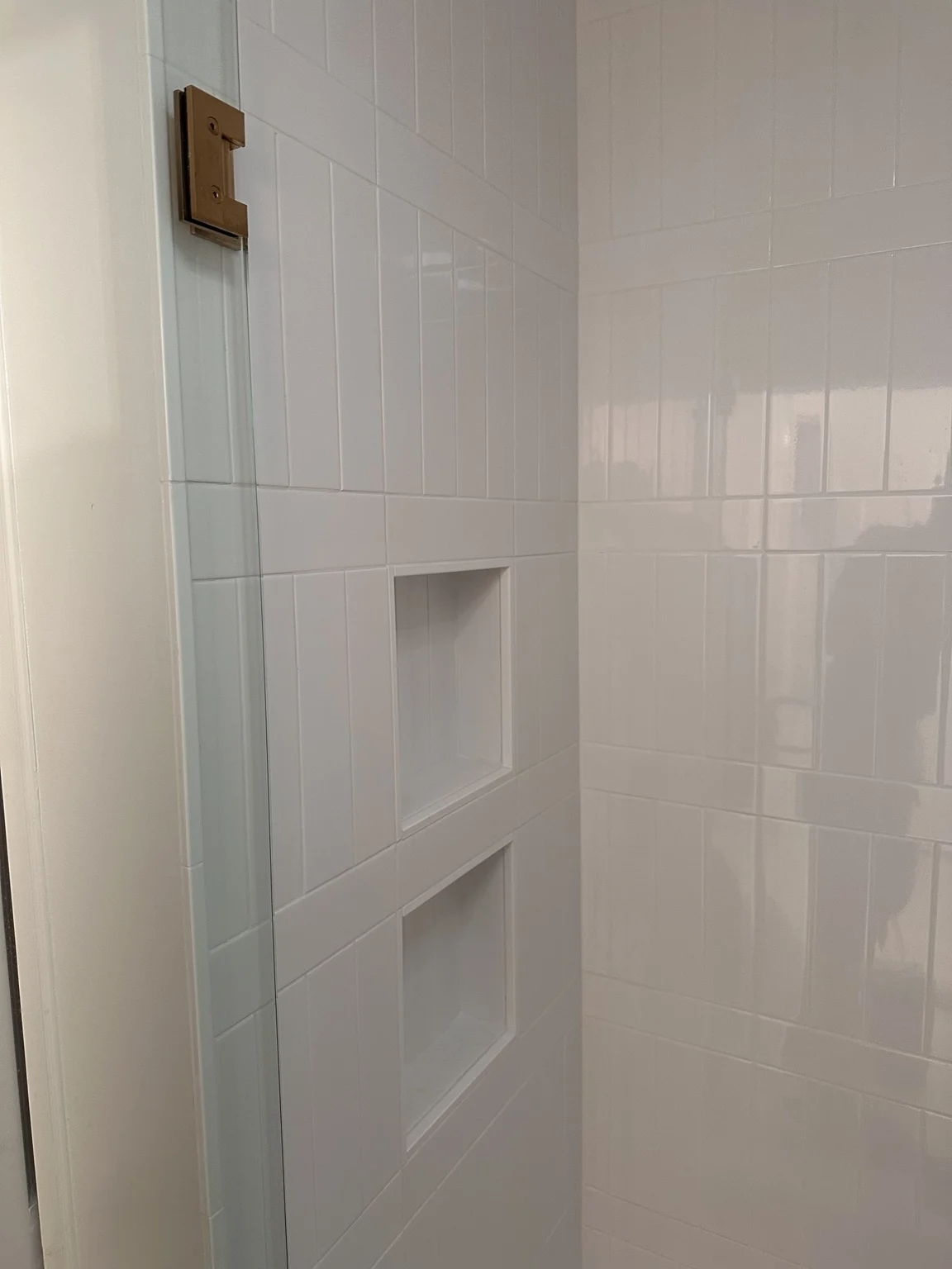 White vertical shower tile with two recessed niches and glass enclosure